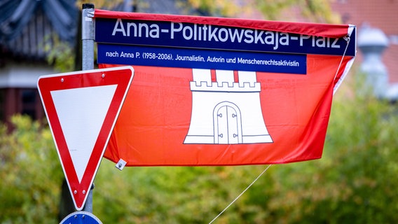 Ein in eine Flagge Hamburgs gehülltes Straßenschild weist auf den Anna-Politkowskaja-Platz hin. © picture alliance/dpa Foto: Axel Heimken