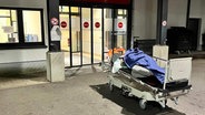 Vor einem Hamburger Krankenhaus liegt ein Obdachloser in einem Bett © Kältebus Hamburg 