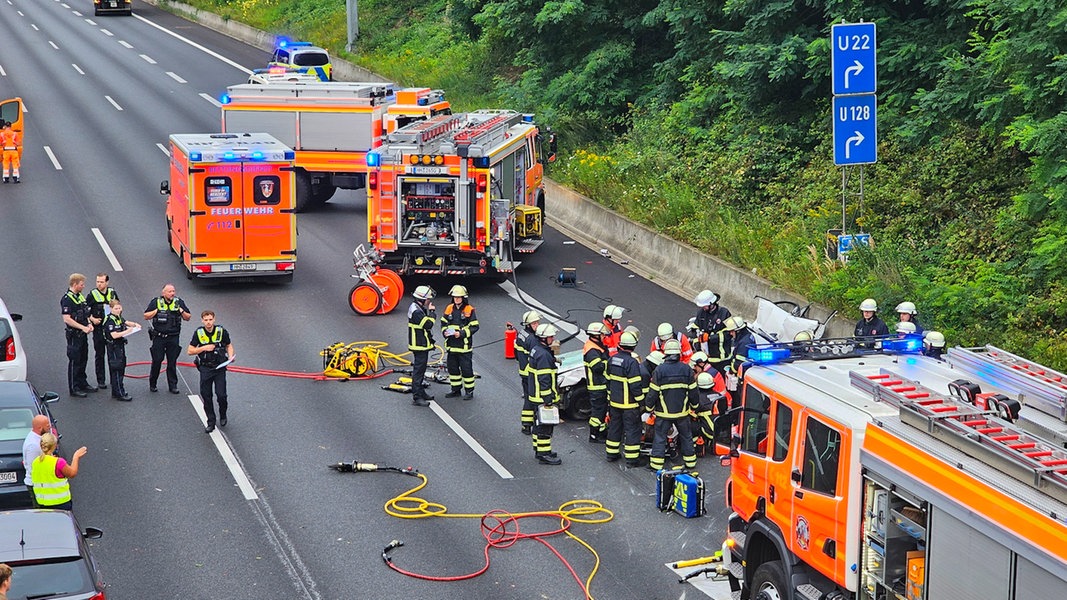 Mehrere Feuerwehreinsatzkräfte stehen auf der Autobahn A1 um ein weißes Auto. 