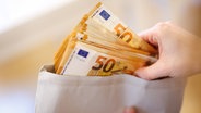 Eine Hand greift in einen Umschlag mit vielen 50-Euro-Scheinen. © dpa Foto: Matthias Balk