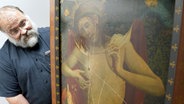 Küster Martin Meier steht neben dem beschädigten Gemälde "Christus als Schmerzensmann" in einem Raum in der Hamburger Hauptkirche St. Petri. © picture alliance / dpa Foto: Marcus Brandt