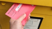 Ein Mann wirft einen Umschlag mit den Briefwahlunterlagen zur Bundestagswahl in einen Briefkasten der Deutschen Post. © IMAGO / Hanno Bode 