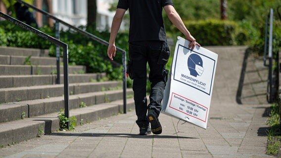 Ein Mann bringt ein abgehängtes Hinweisschild zur Maskenpflicht zu seinem Fahrzeug. © picture alliance/dpa Foto: Daniel Reinhardt