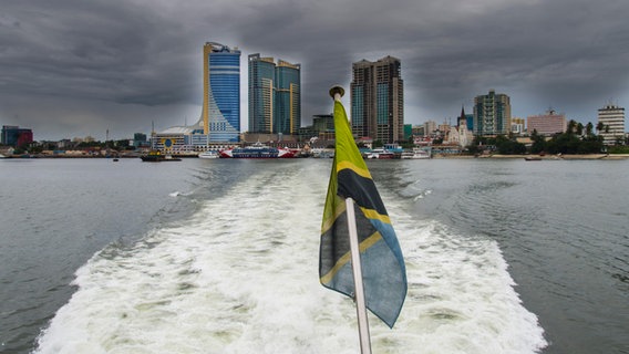 Blick auf das Zentrum von Dar Es Salaam. Im Vordergrund die Flagge Tansanias am Heck eines Bootes. © picture alliance / Avalon Foto: Fredy Mercay