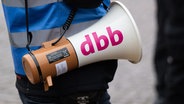 Ein Teilnehmender einer Demo hat ein Handmegaphone umhängen, auf dem der Schriftzug des Beamtenbundes dbb zu sehen ist. (Archivfoto) © picture alliance/dpa Foto: Robert Michael