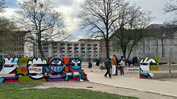 Menschen stehen hinter einem bunt bemalten Sichtschutz vor der Drogeneinrichtung Drob Inn in Hamburg. © NDR Foto: Alexander Heinz