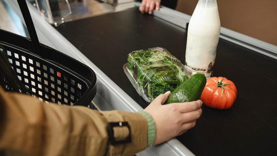 Eine Frau legt im Supermarkt Waren auf das Band. © Westend61 