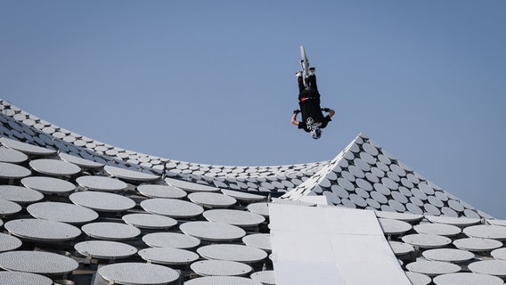 Der Mountainbike-Fahrer Fabio Wibmer macht auf dem Dach der Elbphilharmonie einen Rückwärtssalto mit seinem Rad. © Christian Charisius/dpa 