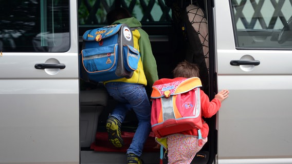 Zwei Kinder mit Schulranzen steigen in ein Auto ein. © dpa Foto: Ralf Hirschberger