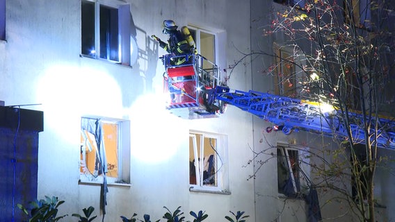 Ein Feuerwehrmann inspiziert ein explodiertes Gebäude von außen über eine Drehleiter © TVNK 