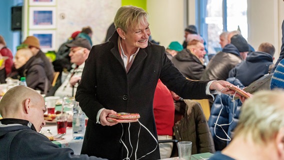 Die Vorsitzende des Rates der Evangelischen Kirche in Deutschland (EKD), Bischöfin Kirsten Fehrs, verteilt auf einer Weihnachtsfeier an Besucher der Tagesaufenthaltsstätte für Obdachlose (TAS) Lebkuchenherzen mit der Aufschrift "Bleib behütet". © picture alliance / dpa Foto: Markus Scholz