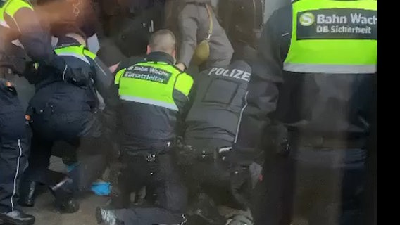 Sechs Mitarbeitende der Polizei und der Hochbahnwache fixieren einen Menschen am Boden. © NDR Foto: Schirin R.