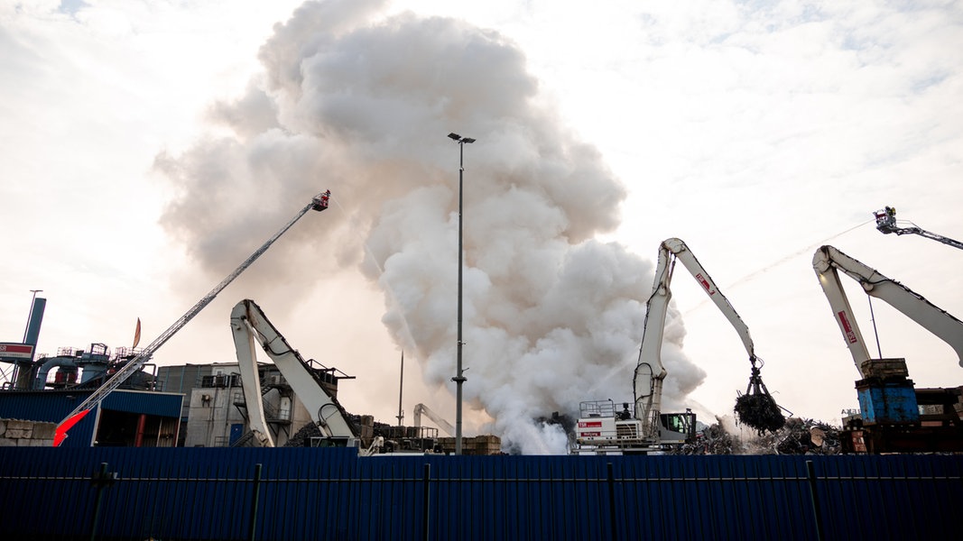 Feuerwehrleute löschen einen brennenden Schrotthaufen im Harburger Hafen.