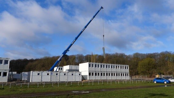 Ein Kran hebt Wohncontainer aufeinander. Auf dem Parkplatz des Volksparkstadions soll ein neues Heim für Geflüchtete entstehen. © picture alliance 