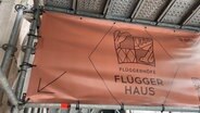 Ein Plakat auf der Baustelle vom Flügger Haus. © Screenshot NDR 