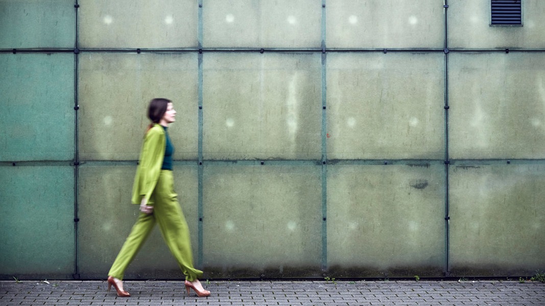 Eine Frau in einem grünen Anzug läuft vor einer Wand.