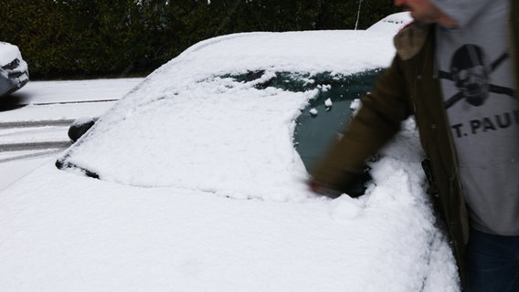 Ein Mann wischt nach starkem Schneefall die Frontscheibe seines Autos frei. © dpa-Bildfunk Foto: Christian Charisius