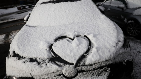 Ein Herz ist auf der schneebedeckten Motorhaube eines geparkten Fahrzeugs zu sehen. © dpa-Bildfunk Foto: Christian Charisius