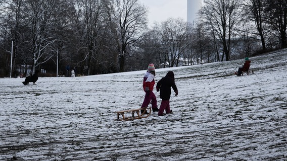 Zahlreiche Menschen sind im schneebedeckten Schanzenpark unterwegs. Auch zwei Kinder die ihren Schlitten hinter sich herziehen. © dpa-Bildfunk Foto: Christian Charisius