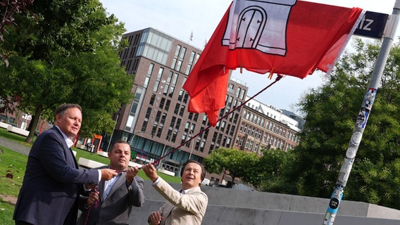 Kultursenator Carsten Brosda (SPD), Ralf Neubauer (SPD), Bezirksamtsleiter Hamburg-Mitte, und Rainer-Maria Weiss, Landesarchäologe Hamburgs, enthüllen das neue Straßenschild mit der Aufschrift Hammaburg-Platz. © dpa Foto: Marcus Brandt