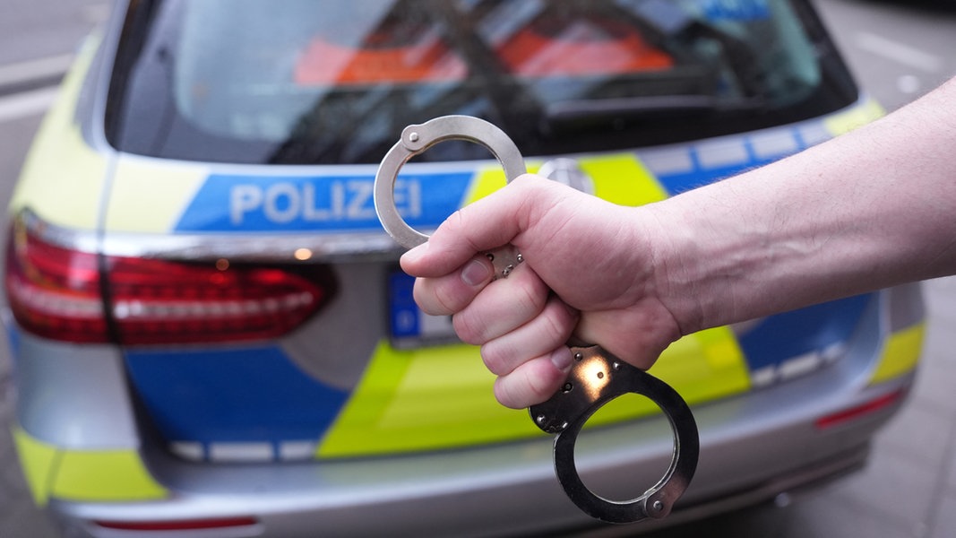 Ein Polizist hält Handschellen vor einem Einsatzfahrzeug hoch.