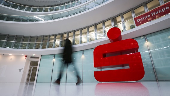 Ein Passant geht an einem großen Sparkassen-Logo vor einer Haspa-Filiale im Deutschlandhaus in der Innenstadt vorbei. © picture alliance/dpa | Christian Charisius Foto: Christian Charisius