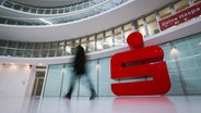 Ein Passant geht an einem großen Sparkassen-Logo vor einer Haspa-Filiale im Deutschlandhaus in der Innenstadt vorbei. © picture alliance/dpa | Christian Charisius Foto: Christian Charisius