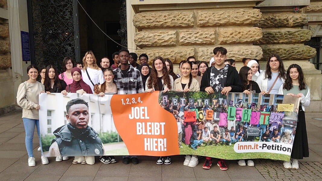 Joel aus Ghana steht mit Mitschülern vor dem Hamburger Rathaus hinter einem Plakat mit der Forderung 