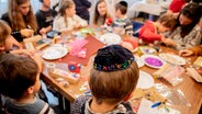 Ein Junge mit einer Kippa basttelt mit anderen Kindern und Erwachsenen an einem Tisch. © picture alliance/dpa | Christoph Soeder Foto: Christoph Soeder