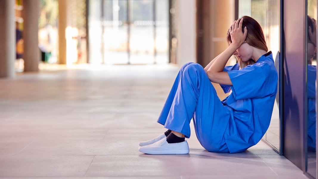 Eine Krankenschwester sitzt auf dem Boden und hält sich die Hände vors Gesicht.