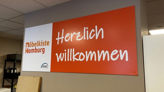 Im Eingangbereich der Möbelkiste Hamburg steht auf einem Plakat "Herzlich Willkommen". © NDR Foto: Screenshot