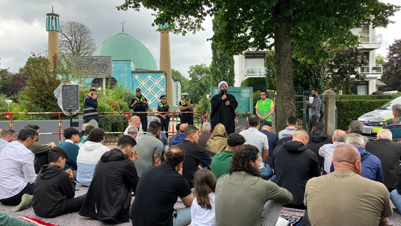 Ein Prediger spricht zu den Gläubigen. Im Hintergrund ist die Blaue Moschee an der Hamburger Außenalster zu sehen, die nach dem IZH-Verbot geschlossen wurde. © dpa Foto: Martin Fischer