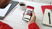 Eine Hand Hält ein Smartphone mit der NDR Hamburg App. © Unsplash / Yura Fresh 