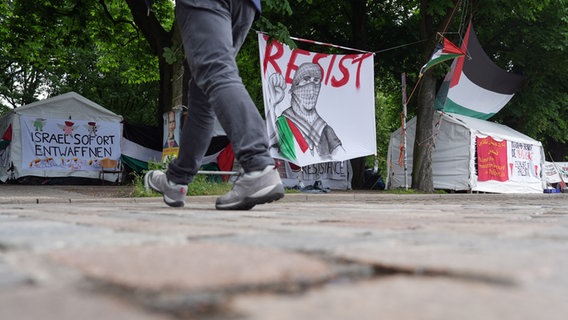 Ein Passant geht an der propalästinensischen Mahnwache nahe der Universität Hamburg auf der Parkanlage Moorweide vorbei. © picture alliance/dpa Foto: Marcus Brandt
