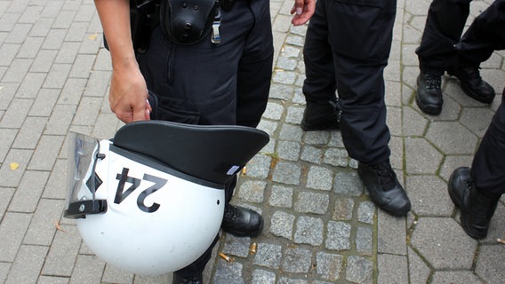 Helm in Hand einer Polizistin und Füße von vier Polizisten. © NDR Foto: Simone Horst