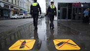 Eine Polizistin und ein Polizist gehen in Hamburg an den neuen Piktogrammen zum Glasflaschen- und Waffenverbot in der Talstraße unweit der Reeperbahn vorbei. © picture alliance / dpa Foto: Marcus Brandt