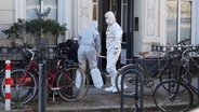 Mitarbeitende der Spurensicherung der Polizei stehen im Stadtteil Hoheluft-West vor einem Mehrfamilienhaus. © Marcus Brandt/dpa 