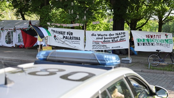 Ein Polizeifahrzeug steht vor Transparenten mit der Aufschrift "Freiheit für Palästina"“, „"die Werte der NATO sind besiegelt mit dem Blut der Syrer, Afghanen, Iraker“" und „"Nieder mit Sozialdemokratischen Pateien, den Dienern des Imperialismus“" bei einer Mahnwache an der Moorweide nahe der Uni Hamburg. © picture alliance/dpa Foto: Christian Charisius