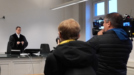 Richter Jan Sturm steht im Ziviljustizgebäude in Hamburg vor der Verkündung des Urteils im Prozess gegen den Impfstoffhersteller Biontech wegen Impfschäden. Im Vordergrund rechts ein Kamerateam. © picture alliance / dpa Foto: Marcus Brandt