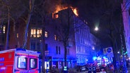 In einer Straße stehen mehrere Einsatzkräfte, die zu einem brennenden Haus schauen. © TV Newskontor 