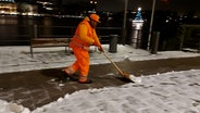 Ein Mitarbeiter der Stadtreinigung in Hamburg schiebt mit einem Schneeschieber Schnee von der Straße. © NDR Foto: Karsten Sekund