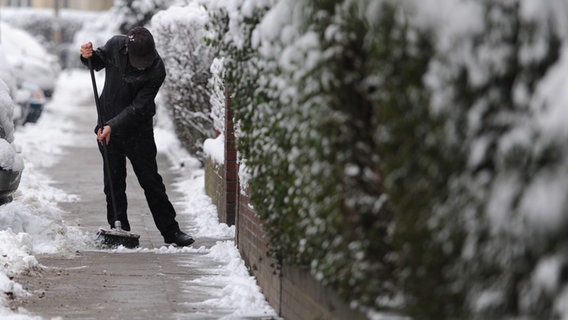 Ein Mann kehrt in Hamburg den Schnee auf einem Gehsteig. © picture alliance / dpa | Angelika Warmuth Foto: Angelika Warmuth