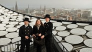 Hamburgs Wirtschaftssenatorin Melanie Leonhard (M.) steht mit zwei Schornsteinfegern auf dem Dach der Elbphilharmonie. © picture alliance / dpa Foto: Christian Charisius