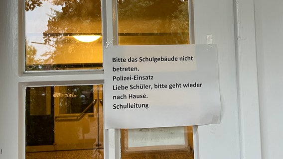 An einer Hamburger Schule hängt ein Zettel auf dem steht: "Bitte das Schulgebäude nicht betreten. Polizei-Einsatz. Liebe Schüler, bitte geht wieder nach Hause. Schulleitung © NDR Foto: Elias Bartl