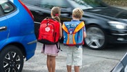 Zwei Kinder stehen mit Schulranzen zwischen Autos und wollen die Straße überqueren. © dpa Foto: Patrick Pleul