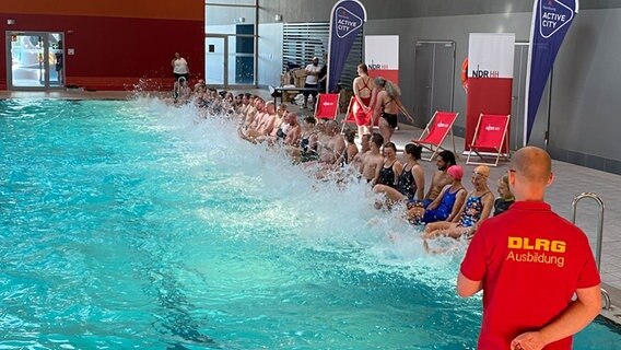 Die neuen Schwimmausbilderinnen und Schwimmausbilder machen Welle, in dem sie mit den Beinen am Beckenrand strampeln. Gleichzeitig ist das eine Übung, durch die Schwimmlehrer Kinder spielerisch ans Wasser gewöhnen. © NDR Foto: Linda Richter