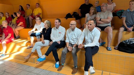 Die Partnerinnen und Partner der  der Aktion "Welle machen"  verfolgen die Abschlussveranstaltung: Hendrik Lünnenburg und Ilka Steinhausen (NDR), Heiko Mählmannn (DLRG), Dirk Schumaier (Bäderland) und Staatsrat für Sport Christoph Holstein. © NDR Foto: Anna Rüter