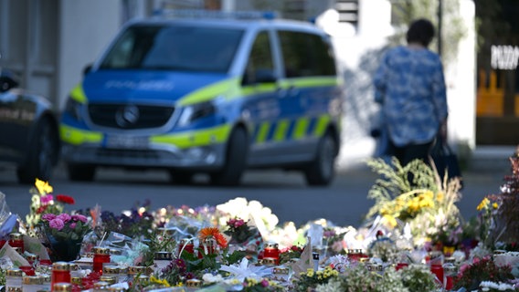 Blumen und Kerzen sind in Solingen zu sehen, dahinter ein Polizeiwagen. Bei einem Stadtfest waren dort drei Menschen mit einem Messer getötet worden. © picture alliance / dpa Foto: Federico Gambarini