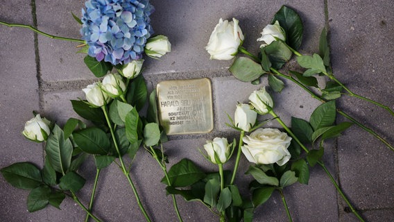 Blumen liegen neben einem Stolperstein vor dem Hotel "Vier Jahreszeiten", der an Harald Seligmann erinnert. © Christian Charisius/dpa 