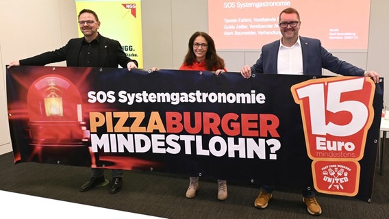 Die DGB-Vorsitzende Yasmin Fahimi,  der NGG-Vorsitzende Guido Zeitler und Verhandlungsführer Mark Baumeister halten ein Banner mit der Aufschrift "SOS Systemgastronomie". © Gewerkschaft Nahrung-Genuss-Gaststätten 